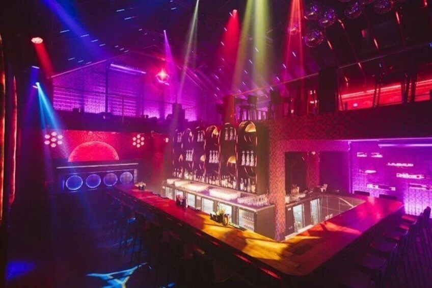 A bar with a neon-lit bar counter and a stage with a red backdrop. 4