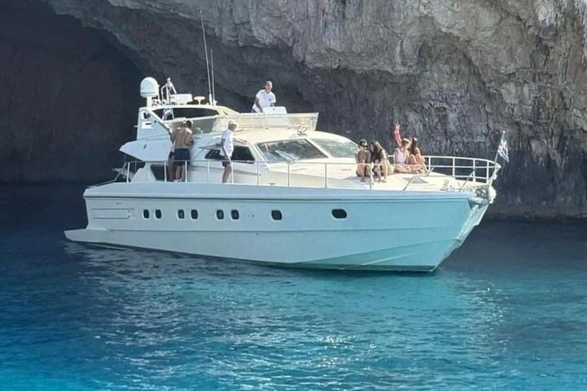 A white yacht with people on deck near a rocky cliff. 2