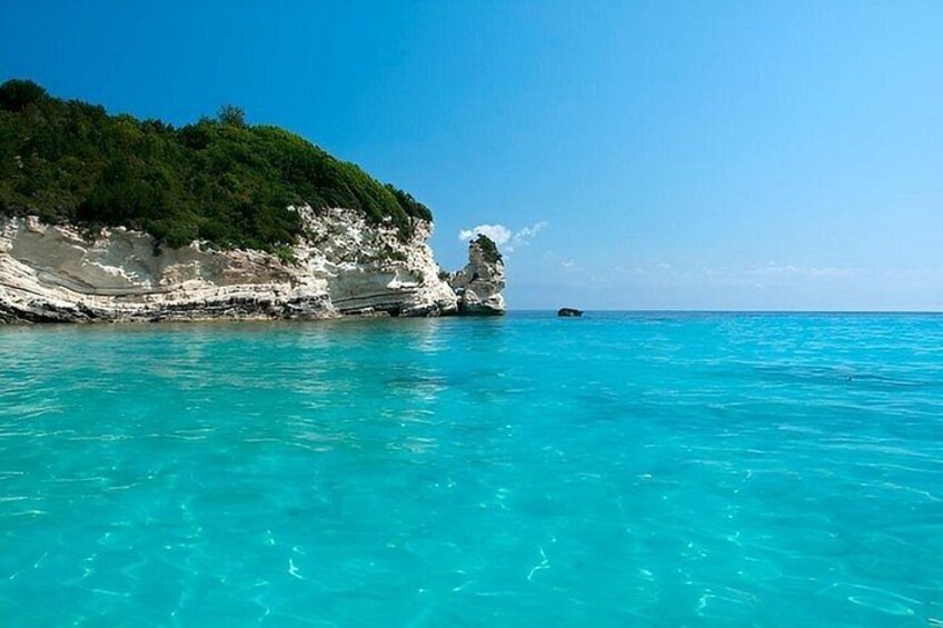 A coastal landscape with clear turquoise waters, white cliffs, and a small rock formation. 4