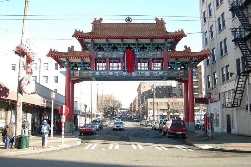 A street with a traditional Chinese archway, cars, buildings, and a crosswalk. 1