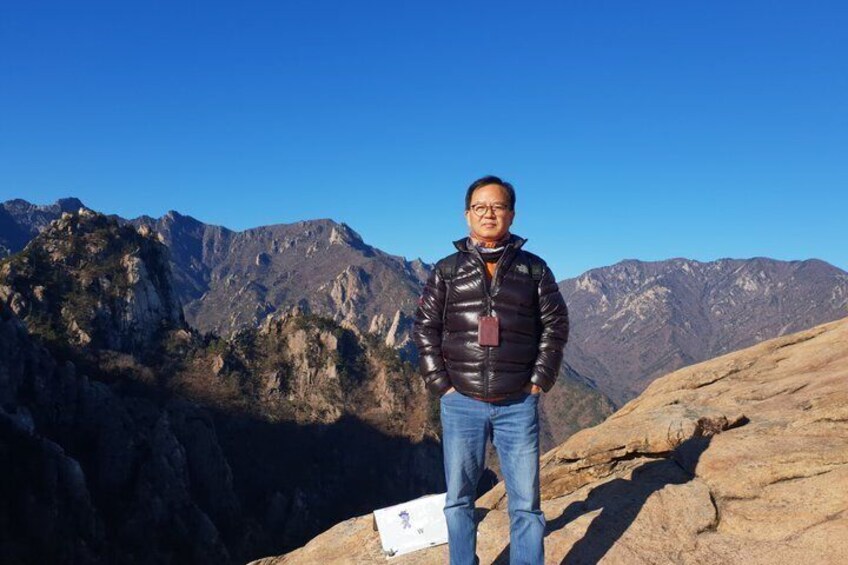 A person standing on a rocky outcrop with a mountainous landscape in the background. 4