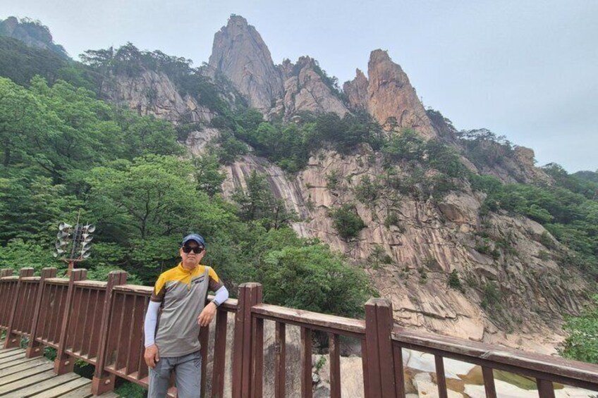 A person standing on a wooden bridge with a mountainous landscape in the background. 2