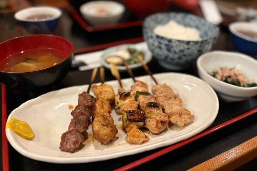 A plate of grilled skewers with meat and vegetables, accompanied by small bowls of dipping sauces and side dishes. 4