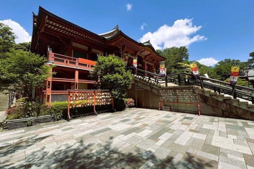 A traditional Japanese temple with a red wooden structure, a stone courtyard, and a clear blue sky. 3