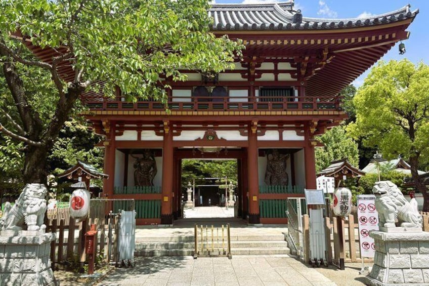 A traditional Japanese gate with a red and white structure, surrounded by stone lanterns and a large tree. 2