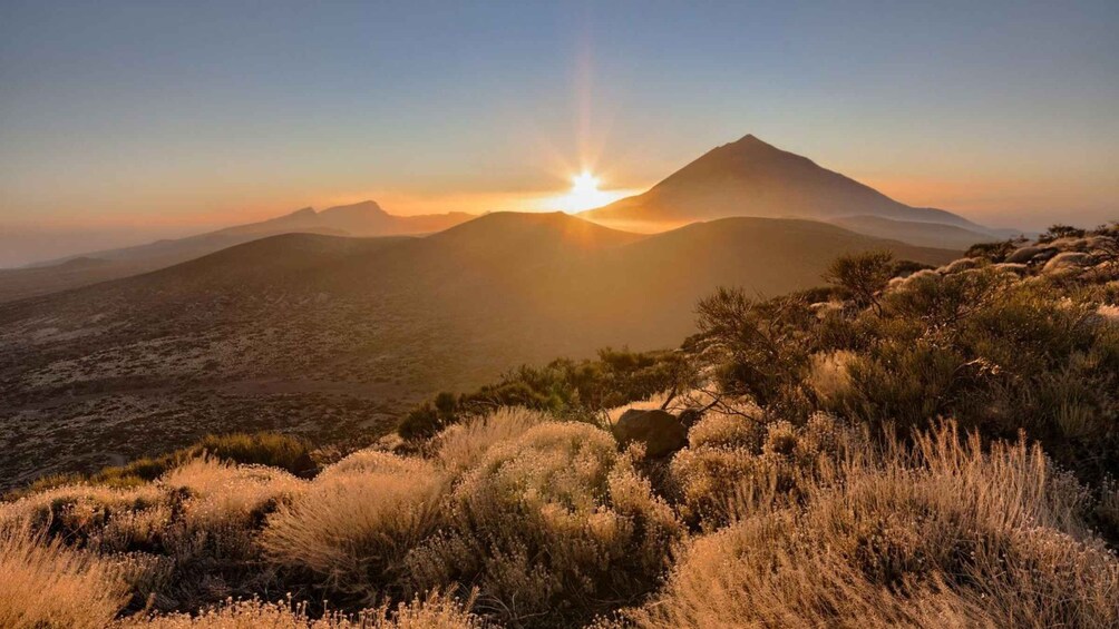 A mountain landscape with a sunrise or sunset, dry grass, and a clear sky. 1
