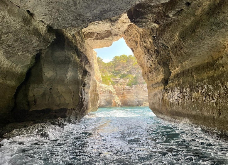 A rocky cave opening to a turquoise sea with a clear sky above. 1