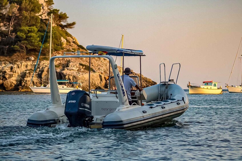 A motorboat with a Yamaha outboard on calm water, a man steering, and a rocky shoreline with trees in the background. 3