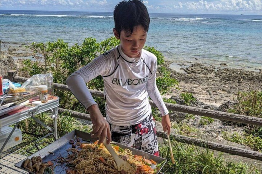 A person cooking noodles by a beach with the ocean in the background. 3