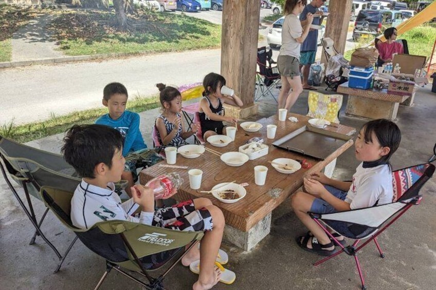 Children sitting at a wooden table outdoors, eating and chatting. 2