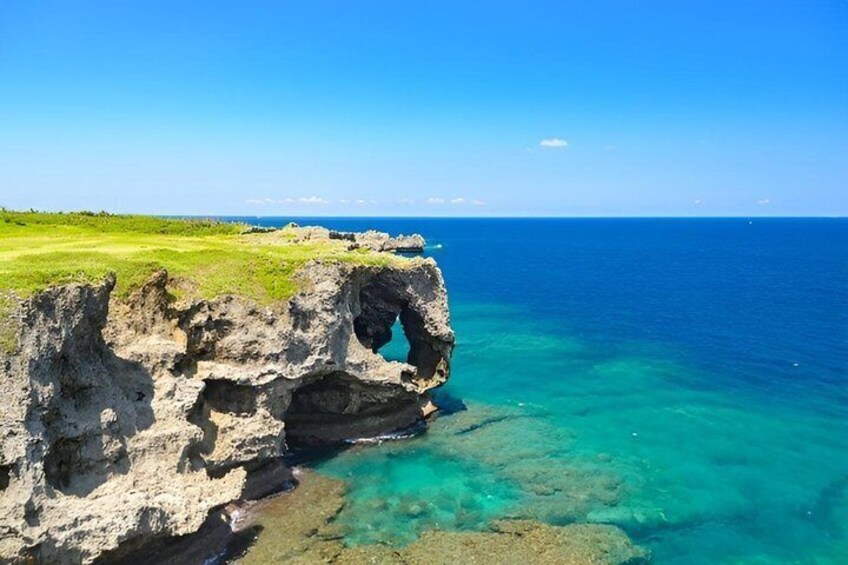 A coastal landscape with a prominent rock formation featuring a natural arch and clear turquoise waters. 5