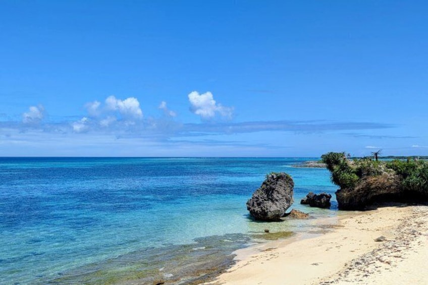 A clear blue sea, a sandy beach, and a rocky outcrop with vegetation. 1