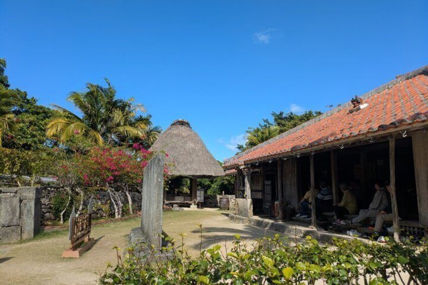 A traditional thatched-roof hut, a covered wooden structure, and a stone wall in a tropical garden setting. 2
