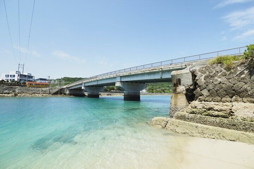 A bridge over clear water, a rocky shoreline, and a building in the background. 3