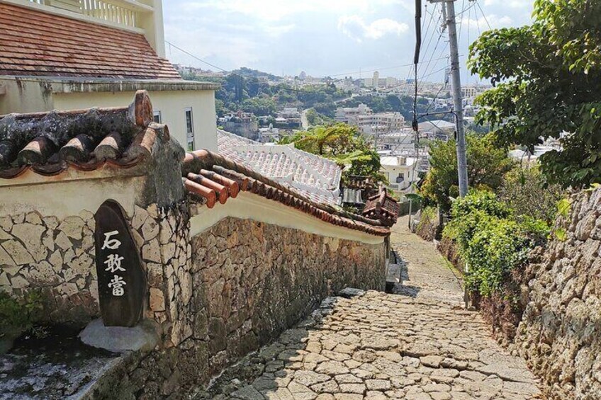A stone staircase leading up a hill, a traditional tiled roof, and a sign with Japanese characters. 4