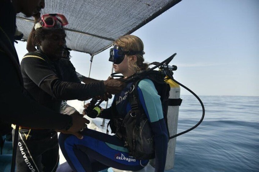 A person in scuba diving gear preparing to enter the water, with a boat and ocean in the background. 5