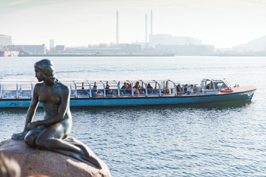 Une statue représentant une figure assise, placée près d’un plan d’eau, avec un bateau en arrière-plan. 3