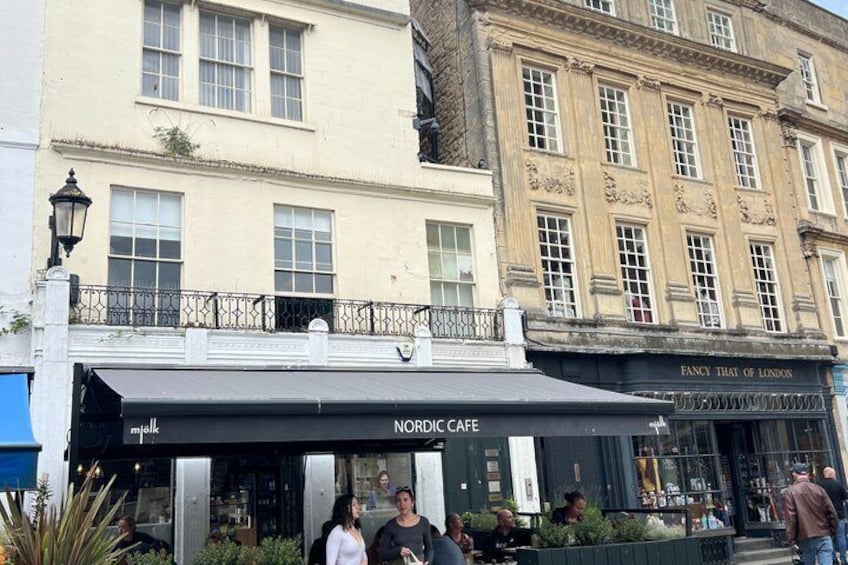 A Nordic Cafe with outdoor seating, a building with 'Fancy That of London' sign, and pedestrians on the street. 2