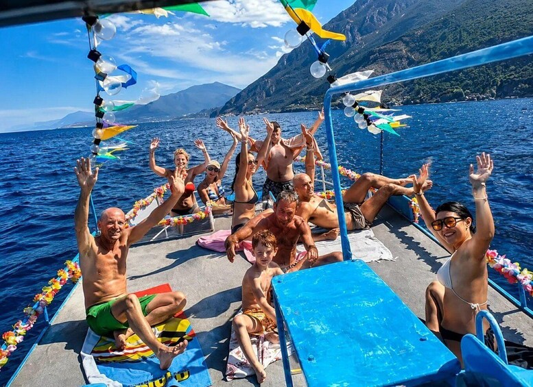 A group of people on a boat with their hands raised, surrounded by colorful decorations and a mountainous landscape in the background. 3