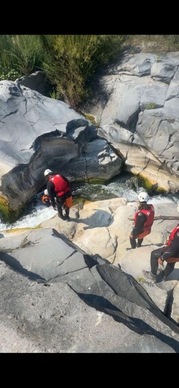 Three individuals in red safety vests and helmets near a rocky stream. 3