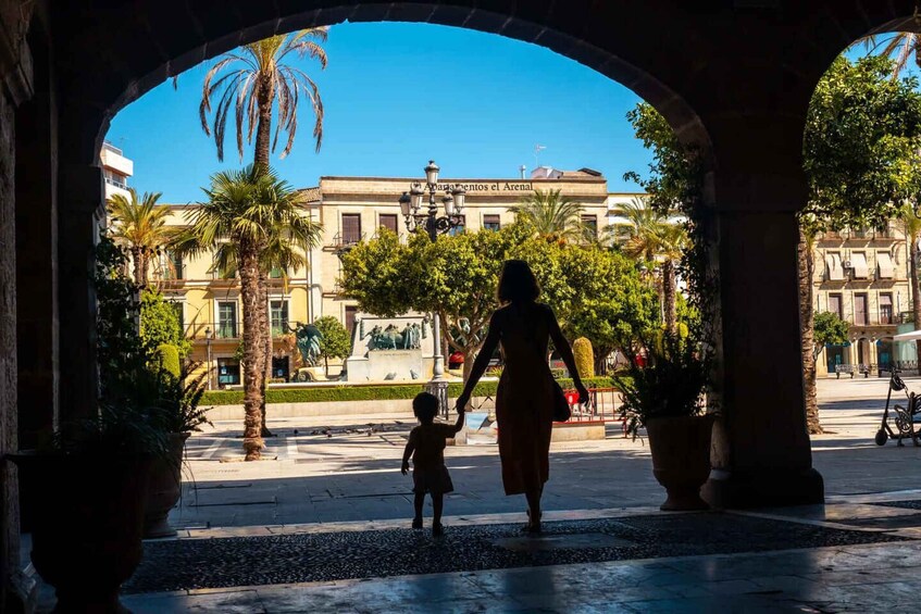 A woman and child walking through an archway with a building labeled 'Abbatia de Sant Pere' in the background. 1