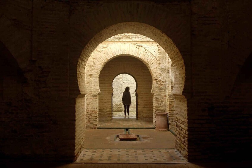 An arched doorway leading to a dimly lit interior space with a person standing at the end of the passageway. 4