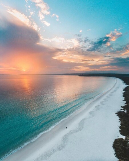 Een strand met iemand die langs de kust wandelt, een heldere lucht en een ondergaande zon. 4