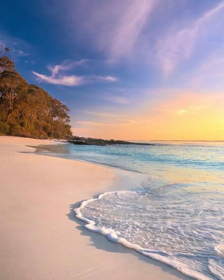 Een strand met helder turquoise water, wit zand en een beboste klif. 2
