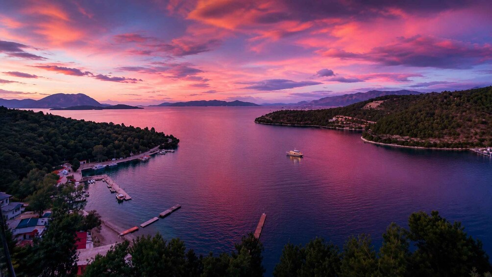 A lake at sunset with a boat, dock, and surrounding forested hills. 2