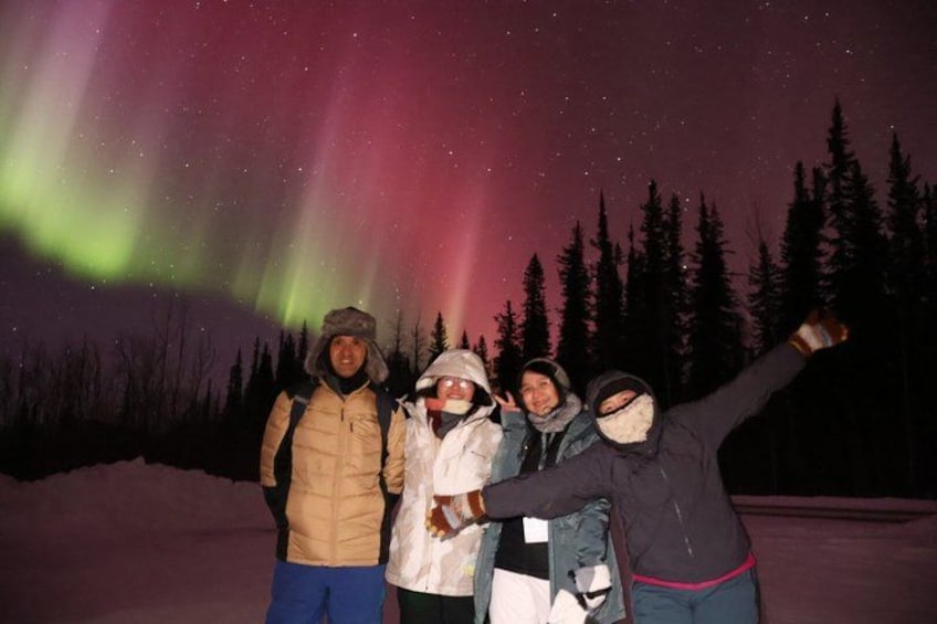 A group of people standing in a snowy landscape with the Northern Lights in the background. 5