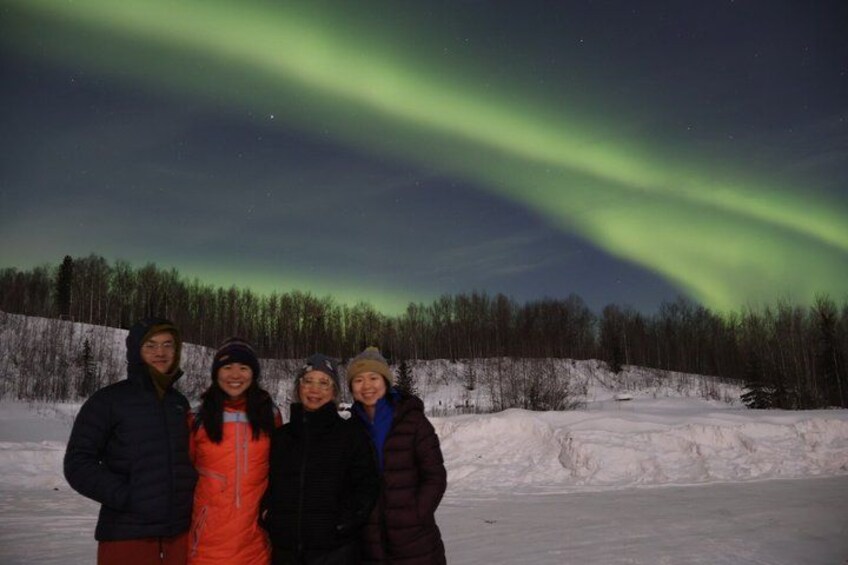 A group of people standing in a snowy landscape with a forest in the background and the aurora borealis in the sky. 3