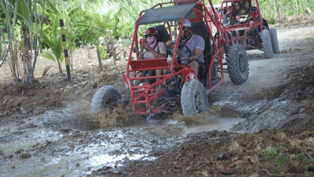 A red off-road vehicle navigating muddy terrain with passengers. 1
