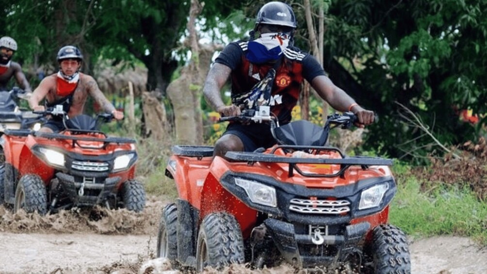 Three people riding off-road ATVs on a muddy trail surrounded by trees. 5