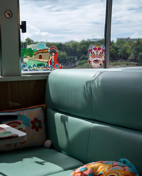A teal sofa with colorful cushions, a window with a view of greenery and a building, and a sticker of a cartoon character. 2