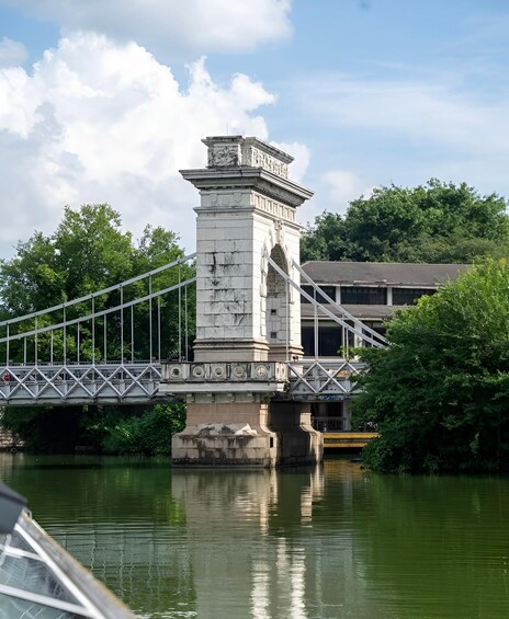 A stone bridge with a central tower over a river, surrounded by trees and a building in the background. 3
