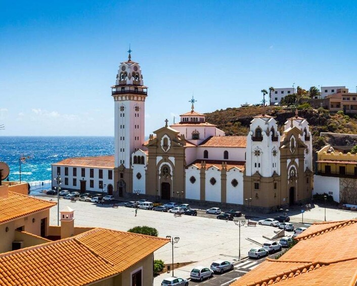 A coastal town with a prominent church featuring a bell tower, a clear blue sky, and the ocean in the background. 1