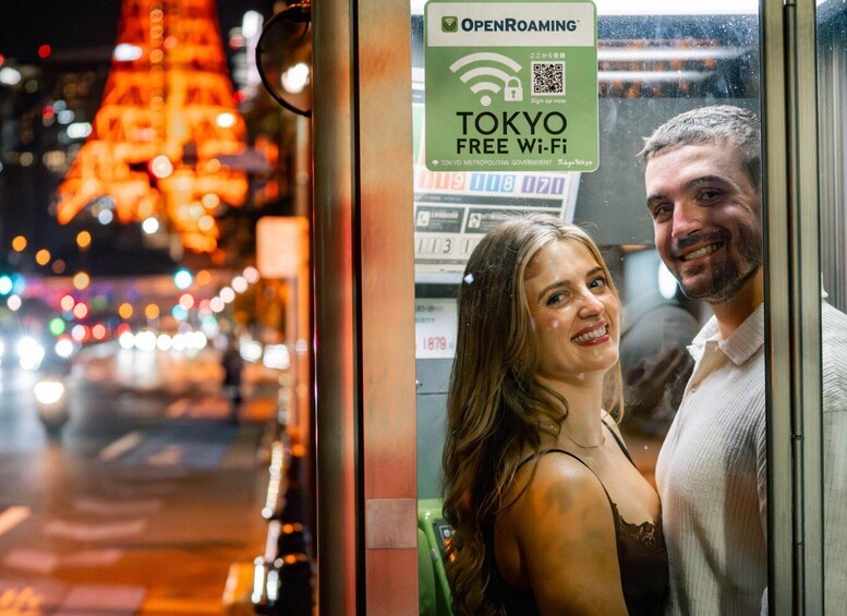 A couple standing in front of a bus with a sign for Tokyo Free Wi-Fi. 1