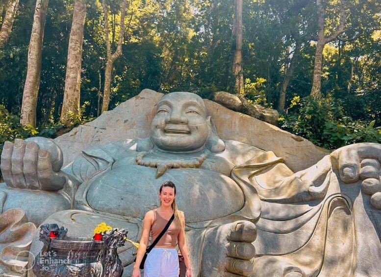 A large stone statue of a laughing Buddha in a forested area. 2