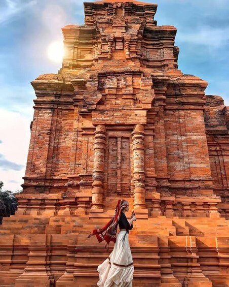 A person in traditional attire standing in front of a large, ancient brick temple with multiple tiers and columns. 1