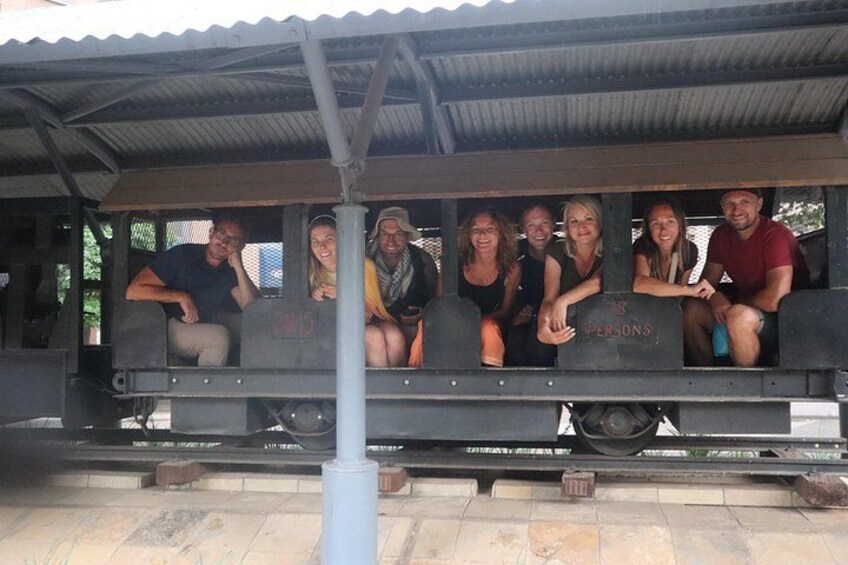 A group of people sitting on a train car labeled 'PERSONS' with a metal roof overhead. 5