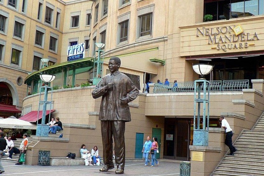 A statue of a man in a suit, Nelson Mandela Square, with people sitting and walking around. 4