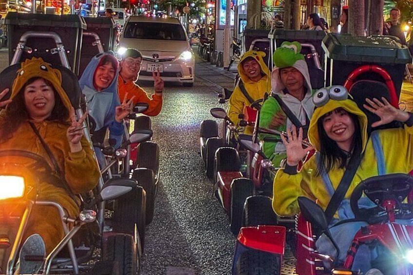 People riding small vehicles on a street with other vehicles and buildings in the background. 5