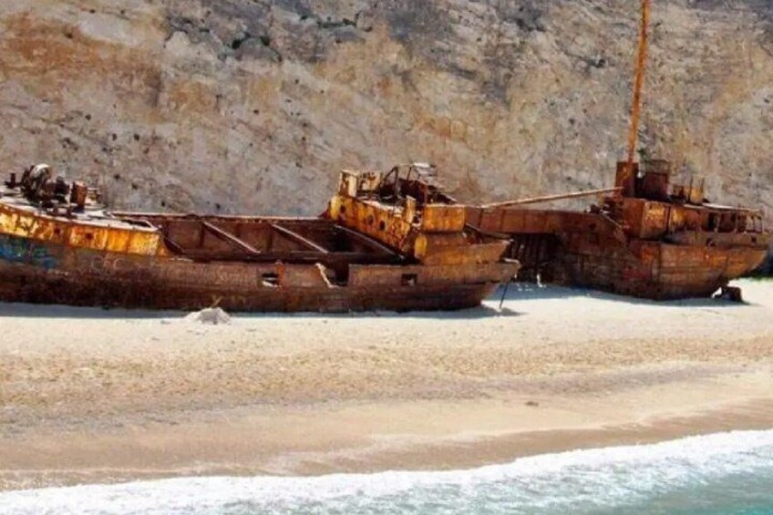 Two rusted ships stranded on a beach with a rocky cliff in the background. 5