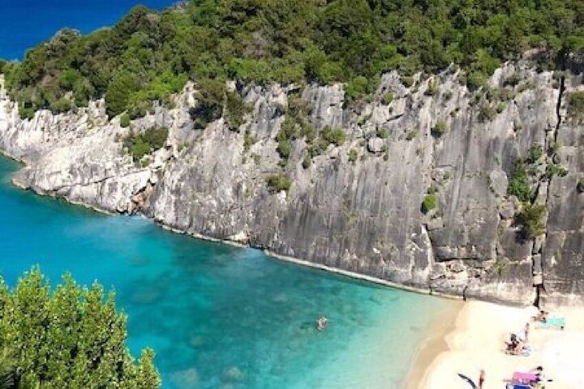 A coastal landscape with clear turquoise waters, rocky cliffs, and a sandy beach. 3