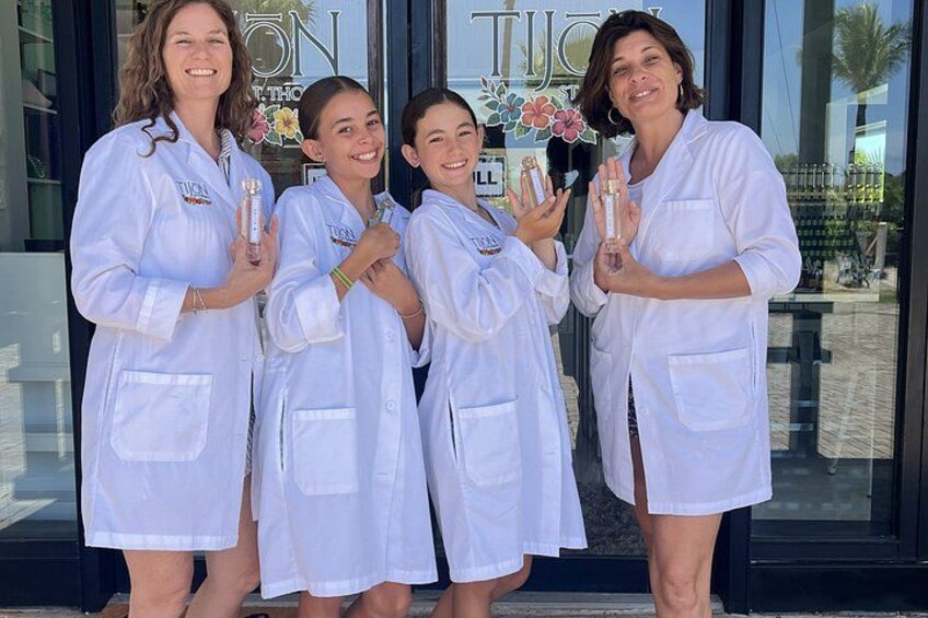 Four people in white lab coats standing in front of a building with a glass door. 5