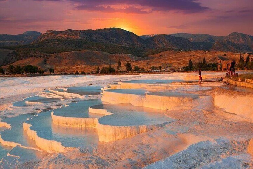Terraced mineral pools, a sunset, and mountains in the background. 1