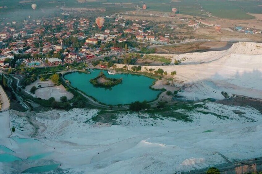 An aerial view of a town with a turquoise lake, white cliffs, and a hot air balloon in the distance. 3
