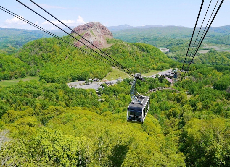 A cable car suspended over a lush green valley with a mountain in the background. 2