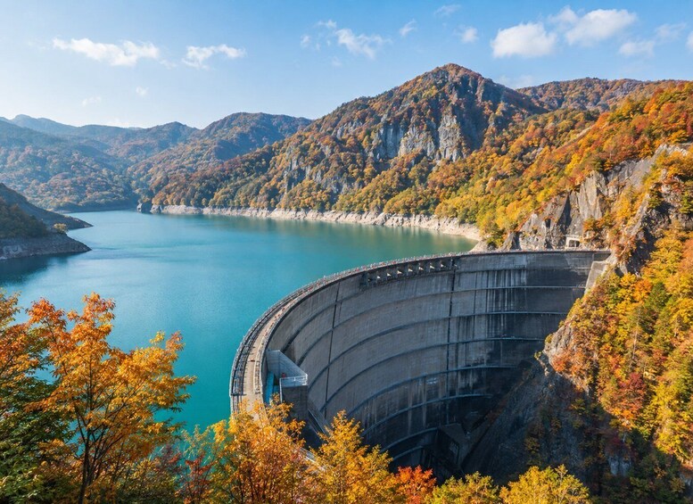 A dam with a curved structure, a lake, and surrounding autumn-colored trees. 2