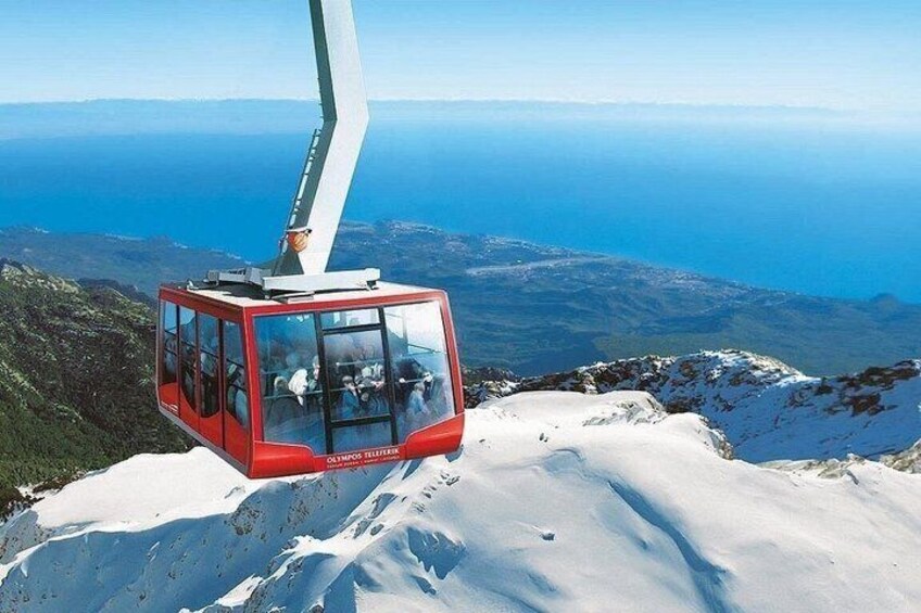 A red cable car on a snowy mountain with a view of the ocean. 2